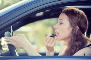 young woman applying lipstick while driving a car