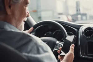 older man driving and looking at phone